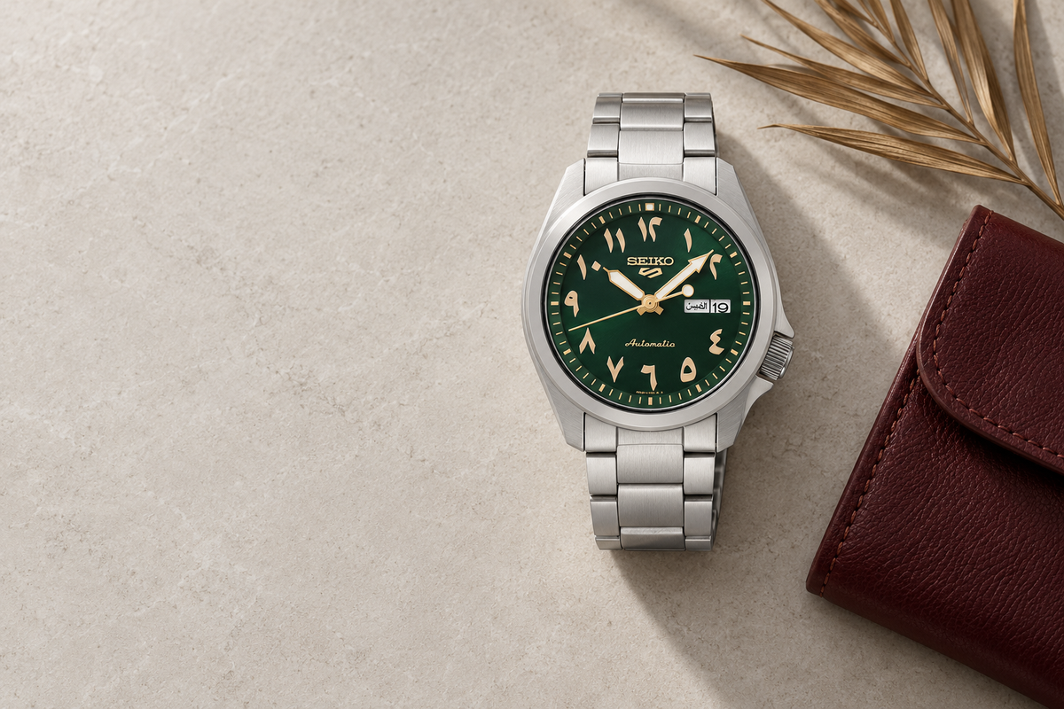 Seiko 5 Arabic green dial watch on light stone with a burgundy leather pouch and date palm frond